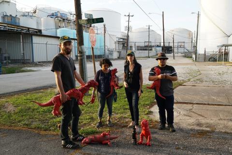 Four people stand in the street holding red plastic dinosaurs